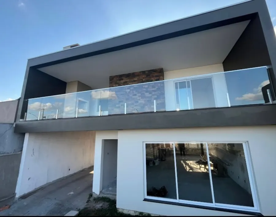 Casa em obra com esquadrias brancas e guarda-corpo de vidro na sacada
