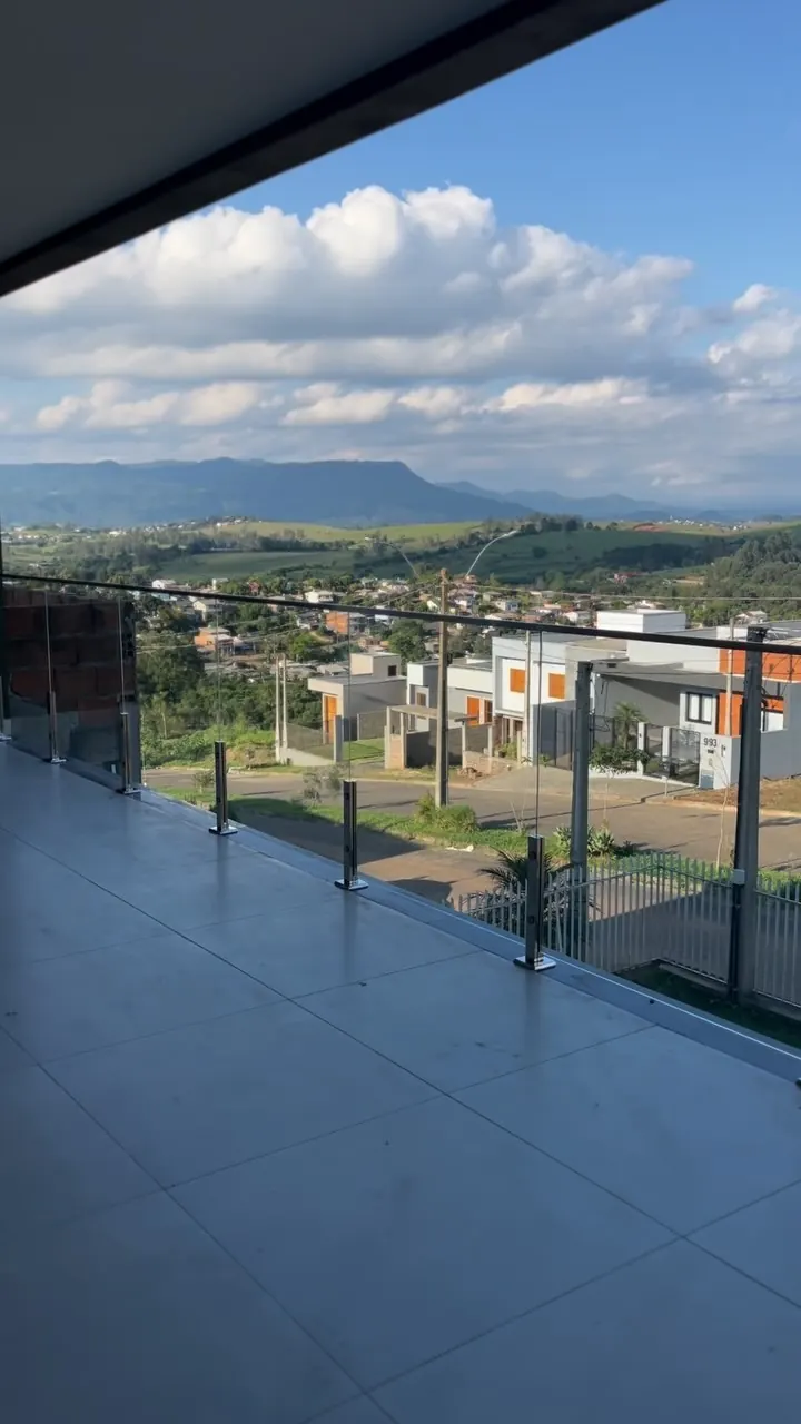 Sacada com guarda-corpo de vidro e pinças de inox com vista para morros