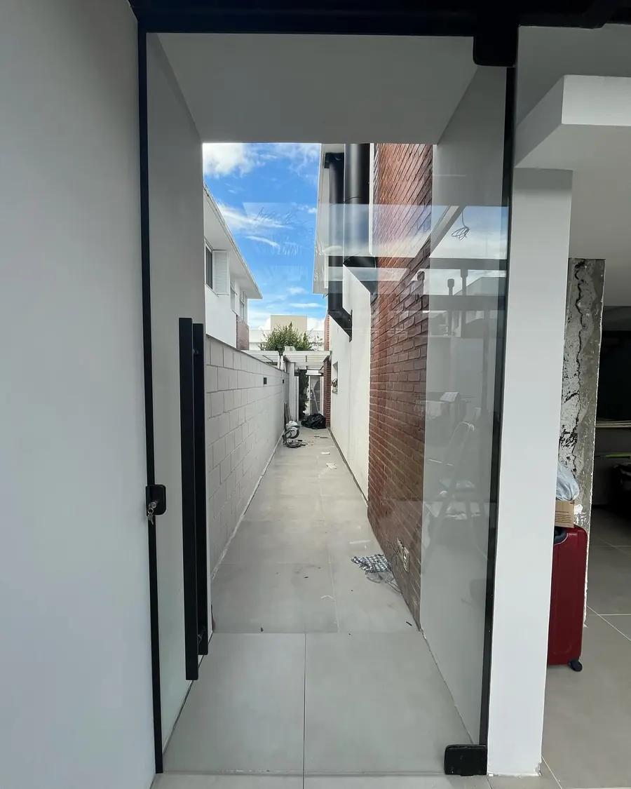 Porta pivotante de vidro com acabamento preto em corredor lateral