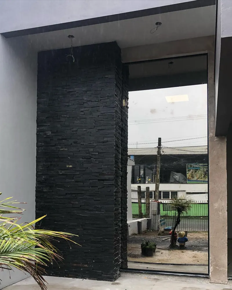Fachada fixa em vidro reflecta cinza com alumínio preto ao lado de parede de pedra escura