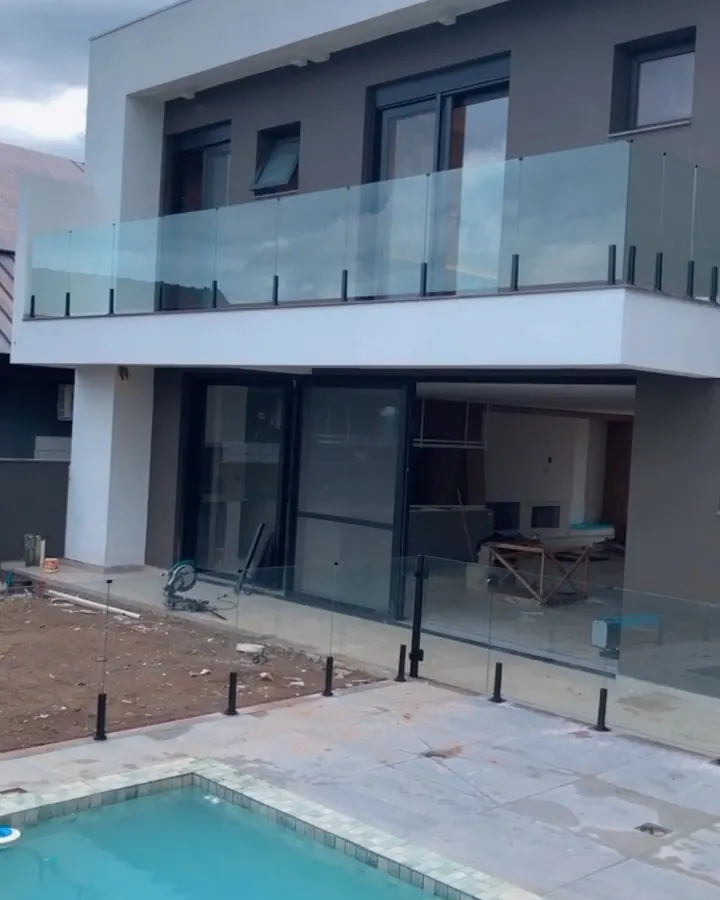 Guarda-corpo de vidro com torres de pinça de inox preto em sacada de casa com piscina
